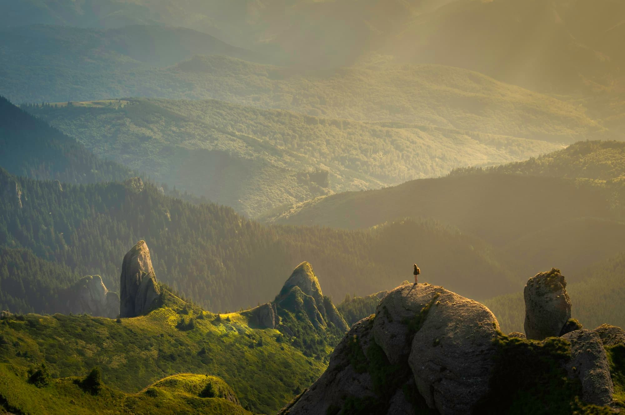 A lone figure on a ridge above sunlit mountain foothills